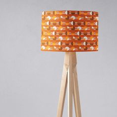 an orange and white lampshade with wooden tripod legs on a grey background