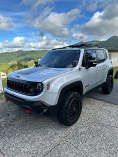 a white jeep parked on the side of a road next to a hill with clouds in the sky