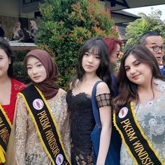 four young women standing next to each other in front of a building with banners on them