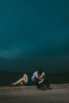 a man and woman sitting on the ground next to each other under a cloudy sky