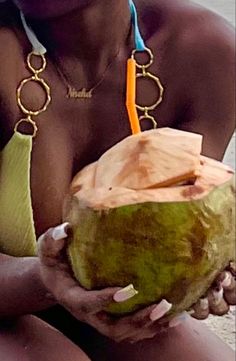 a woman sitting on the beach with a coconut in her hand and wearing a necklace