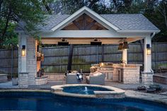 an outdoor kitchen next to a pool in a backyard with a grill and seating area