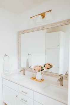 a bathroom with a large mirror and flowers in a vase on the sink counter top