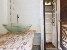 a glass bowl sink sitting on top of a wooden counter next to a doorway with shutters