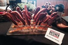 there are many bacon skewers on the table with a sign that says butcher bbq