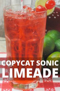 a red and white checkered table cloth with a glass filled with liquid next to limes