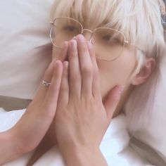 a blonde haired woman wearing glasses covers her face with her hands while laying in bed