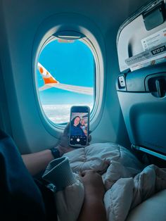 a person taking a photo of an airplane window with their cell phone while sitting in bed