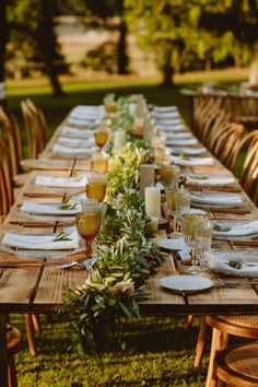 a long wooden table with plates and glasses on it in the middle of a grassy area