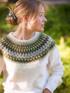 a woman wearing a white sweater with a green and beige pattern on the collar is standing outside