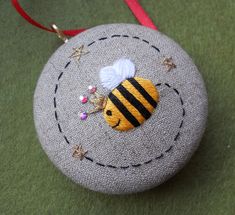 a small round ornament with a bee on it's side, hanging from a red ribbon