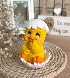 a yellow toy duckling in an egg shell with a white hat on its head