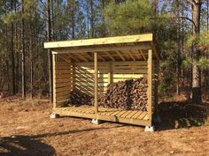 a wooden shelter in the middle of a forest filled with logs and wood stacked on top of each other