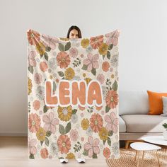 a woman holding up a floral blanket with the word lena on it in front of her