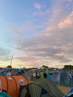 many tents are set up on the ground with people standing around them under a cloudy blue sky