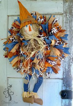 a scarecrow door hanger on the side of a white door with blue, orange and brown decorations