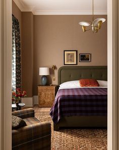 a bed room with a neatly made bed next to a chair and lamps on the wall