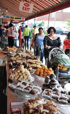 people are standing at an outdoor market with many different types of pastries on display