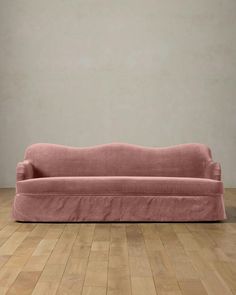 a pink couch sitting on top of a hard wood floor next to a white wall