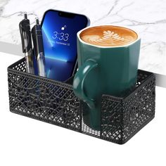 a cup of coffee sitting on top of a desk next to a cell phone and pen