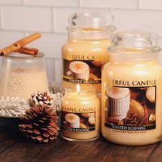 three candles sitting on top of a wooden table next to a pine cone and candle holder