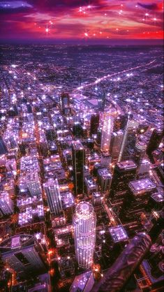 an aerial view of a city at night with bright lights and skyscrapers in the foreground