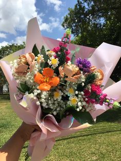 a person holding a bouquet of flowers in their hand with grass and trees in the background