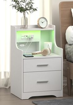 a white nightstand with a clock and plants on it next to a bed in a room