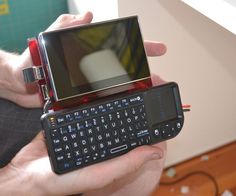 a person holding a cell phone with a keyboard attached to the back of it's case