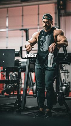 a man standing in front of a gym machine holding a water bottle and looking at the camera