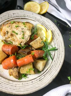 a white plate topped with chicken, potatoes and carrots next to lemon wedges