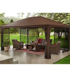 a gazebo sitting on top of a patio next to a lush green field and trees