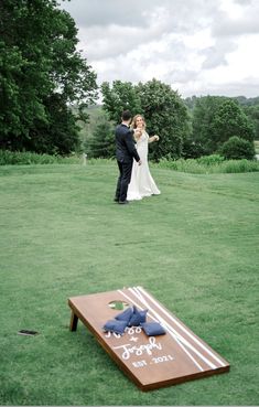 a bride and groom standing in front of a cornhole game on the lawn at their wedding