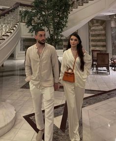 the man and woman are walking down the stairs in their white outfits with brown purses