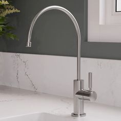 a kitchen sink with a chrome faucet and white marble counter top next to a window