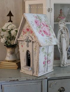 a doll house sitting on top of a dresser next to flowers and an angel figurine