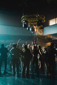 a group of people standing around each other in front of a disco ball with their hands up