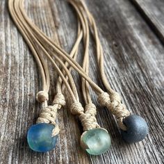 three necklaces on a wooden surface with ropes and beads hanging from them, one is blue and the other is green