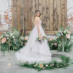 a woman in a wedding dress standing next to flowers and greenery