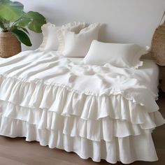 a bed with white ruffled sheets and pillows on it next to a potted plant