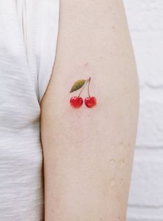 two cherries on the back of a woman's left arm, one with a green leaf