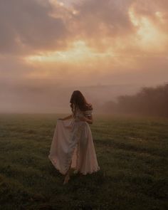 a woman in a white dress is walking through the foggy field with her back to the camera