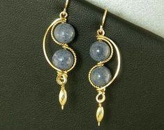 two blue beads are hanging from gold plated hoops on a black leather surface