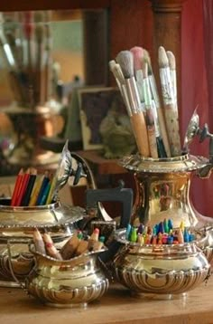 there are many pens and pencils in the silver vase on the table next to the mirror