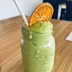 a green smoothie with an orange slice sticking out of it's top on a wooden table