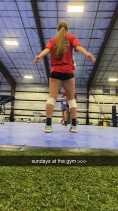 a woman in red shirt and black shorts standing on top of a blue mat with words underneath her