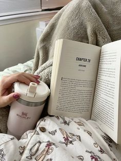 a woman is reading a book while holding a sippy cup