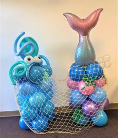 two blue and purple balloons are in a net bag with a mermaid tail on top