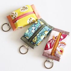 three purses with keychains attached to them on a white surface, one in the shape of a wallet