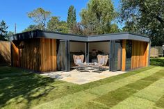 two chairs are sitting in the grass near a shed with wooden walls and doors on it